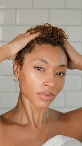 Try on this short curly hairstyle featured on a woman posing in front of a white brick wall.