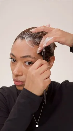 Try on a scene showing a person applying a hair treatment on short, wet hair, with hands visible in the act of smoothing or styling the hair.