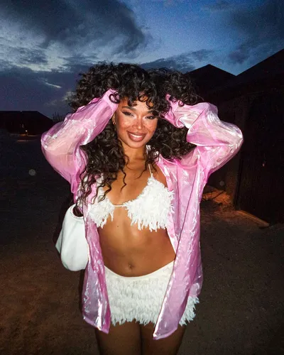 Try on this voluminous long curly hairstyle that cascades freely around the shoulders, highlighted by ambient low light.