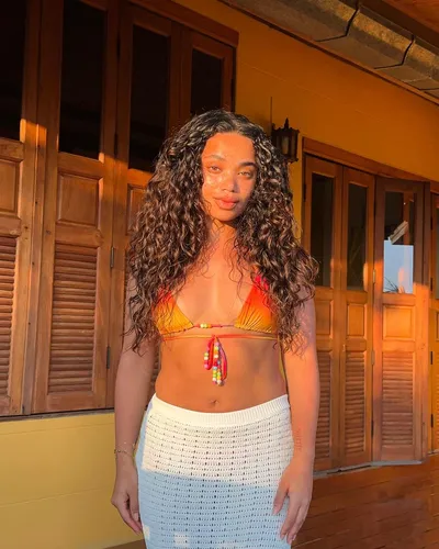 Try on this long curly hairstyle that flows over the shoulders, glistening in natural sunlight.