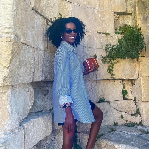 Try on this medium length curly hairstyle as showcased by the smiling woman standing against a stone wall.
