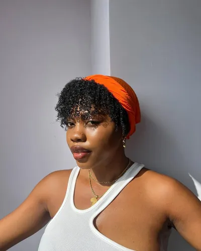 Try on a short curly hairstyle with wispy curls framing the face, accessorized with a bright orange headscarf.