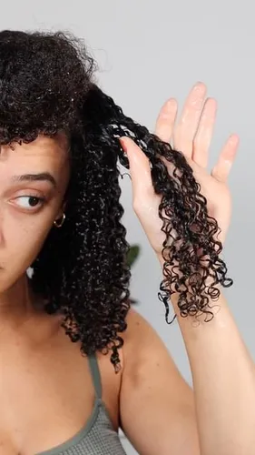 Try on this curly hairstyle featuring tight, springy curls that cascade down one side while being held by the hand. The focus on the texture and style makes it a great reference for curly hair treatments or styling.