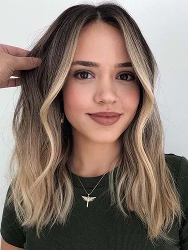 Try on this popular hairstyle featuring a wavy, ombre look with dark roots transitioning into lighter blonde tips.