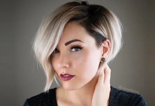 Try on this stylish asymmetric bob cut with side-swept bangs and two-tone color highlighting a dramatic contrast between blonde and dark roots.