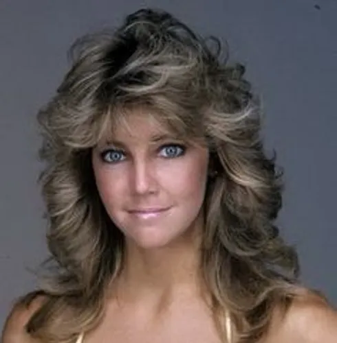 Try on this voluminous curly hairstyle that features large, bouncy curls with a lot of body and texture, complemented by feathered layers that frame the face beautifully.