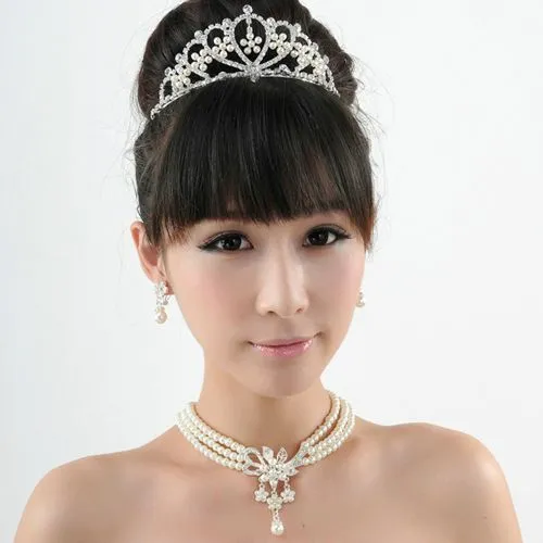 Try on this elegant updo hairstyle complemented by sleek bangs, adorned with a sparkling tiara