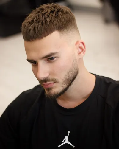 Try on a short hairstyle featuring a textured top with a fade on the sides and back, complemented by a neatly trimmed beard.
