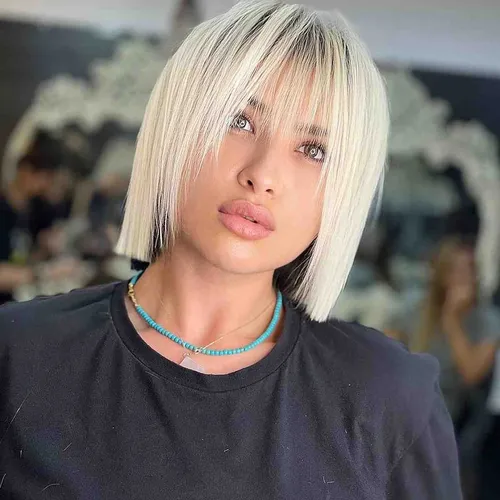 Try on this chic platinum blonde blunt bob hairstyle, featuring a sleek and straight cut just at the jawline, complemented by a subtle fringe.