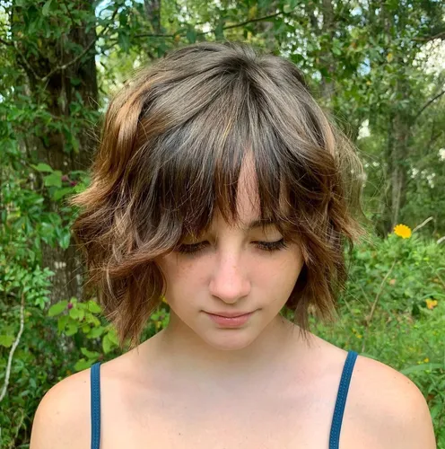 Try on a textured shaggy hairstyle with bangs framing the face, highlighting a casual and youthful look.