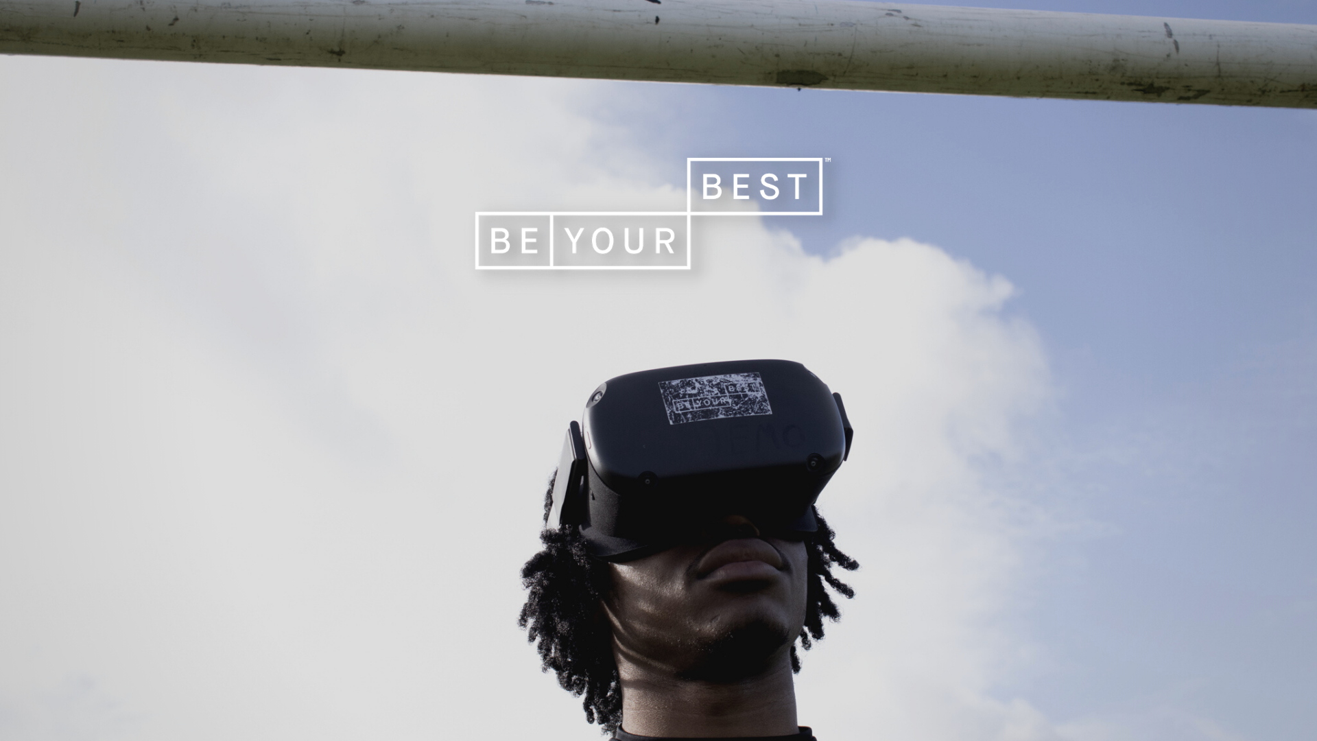 Male wearing VR headset, standing outside and underneath the crossbar of some football goalposts